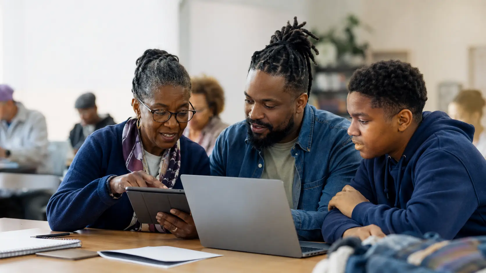 An older adult, an adult facilitator, and a teen learning together with a tablet and laptop